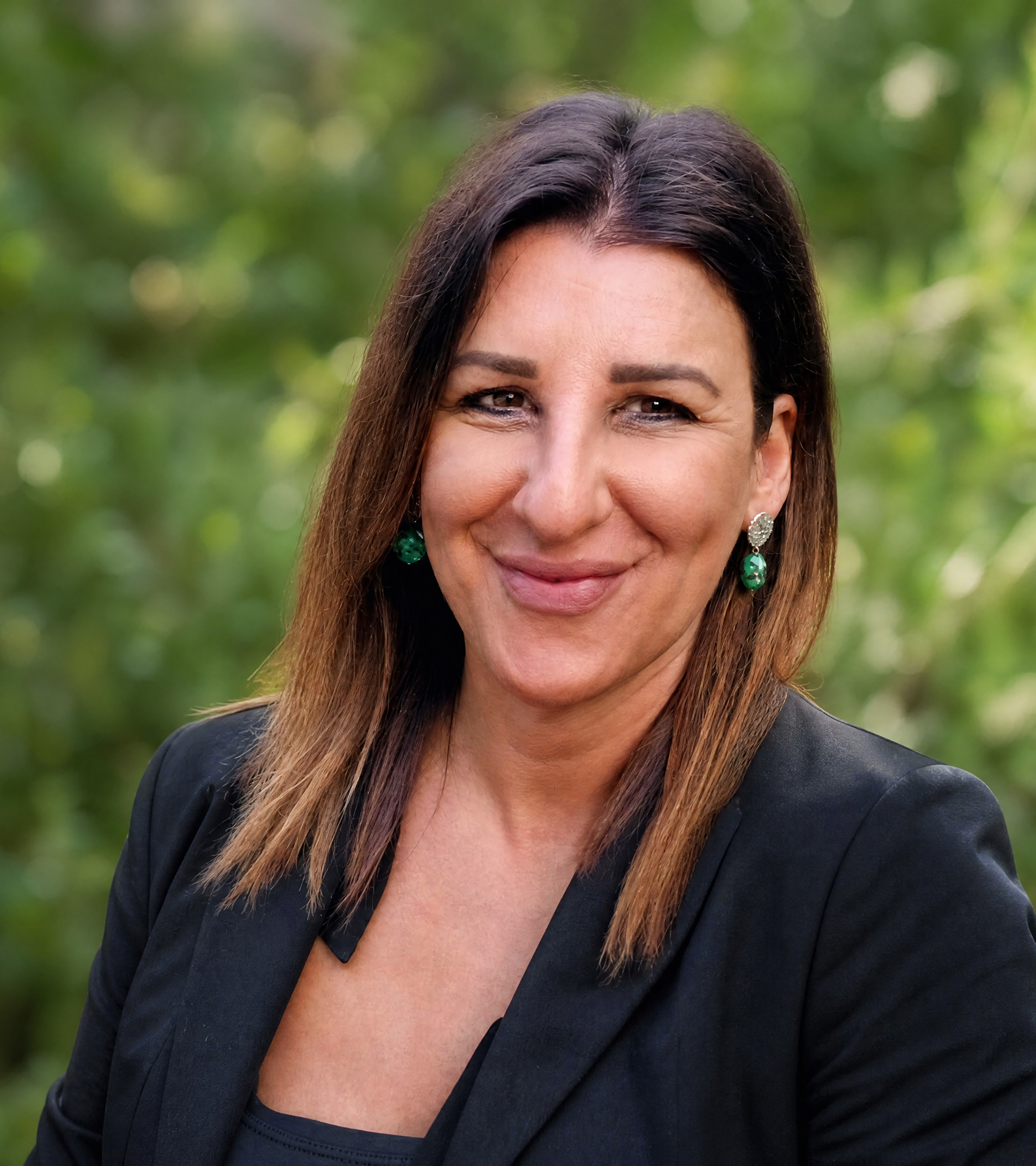 Professional portrait of Grazia Polidori against a softly blurred natural green background.